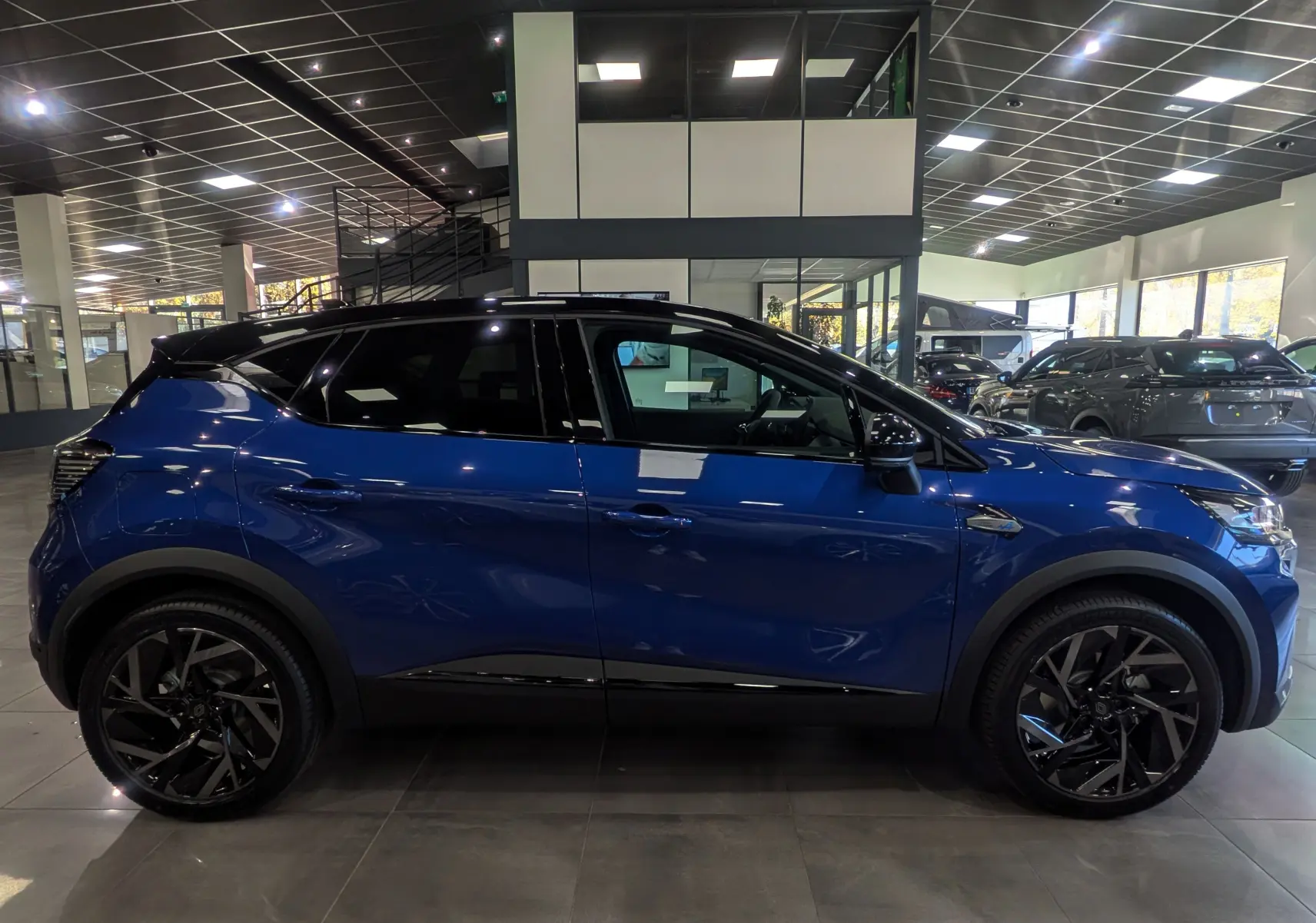Profil côté gauche du Renault Captur E-TECH 160 esprit Alpine bleu Iron avec toit noir et jantes noires en showroom.