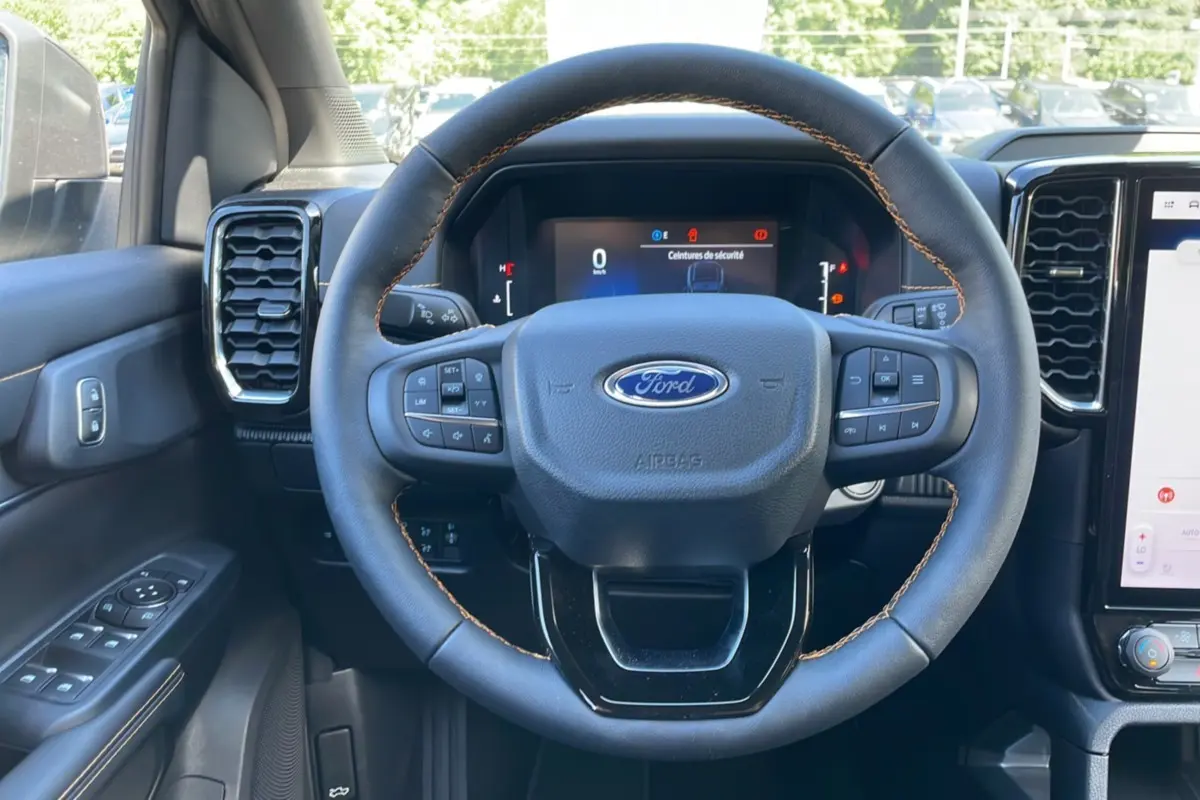 Vue centrée sur le volant cuir noir avec surpiqûres marron du Ford Ranger 2026, tableau de bord digital et commandes au volant visibles.