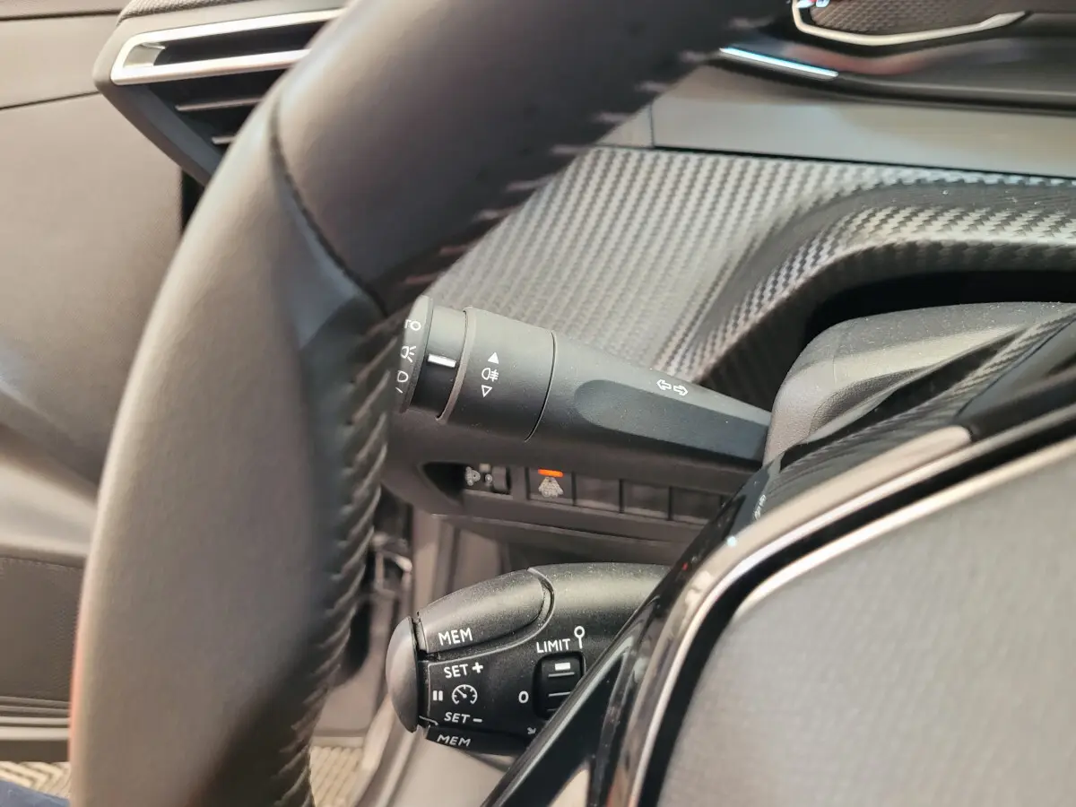 Gros plan sur le volant cuir et les commandes de régulateur de vitesse côté gauche du tableau de bord gris foncé.