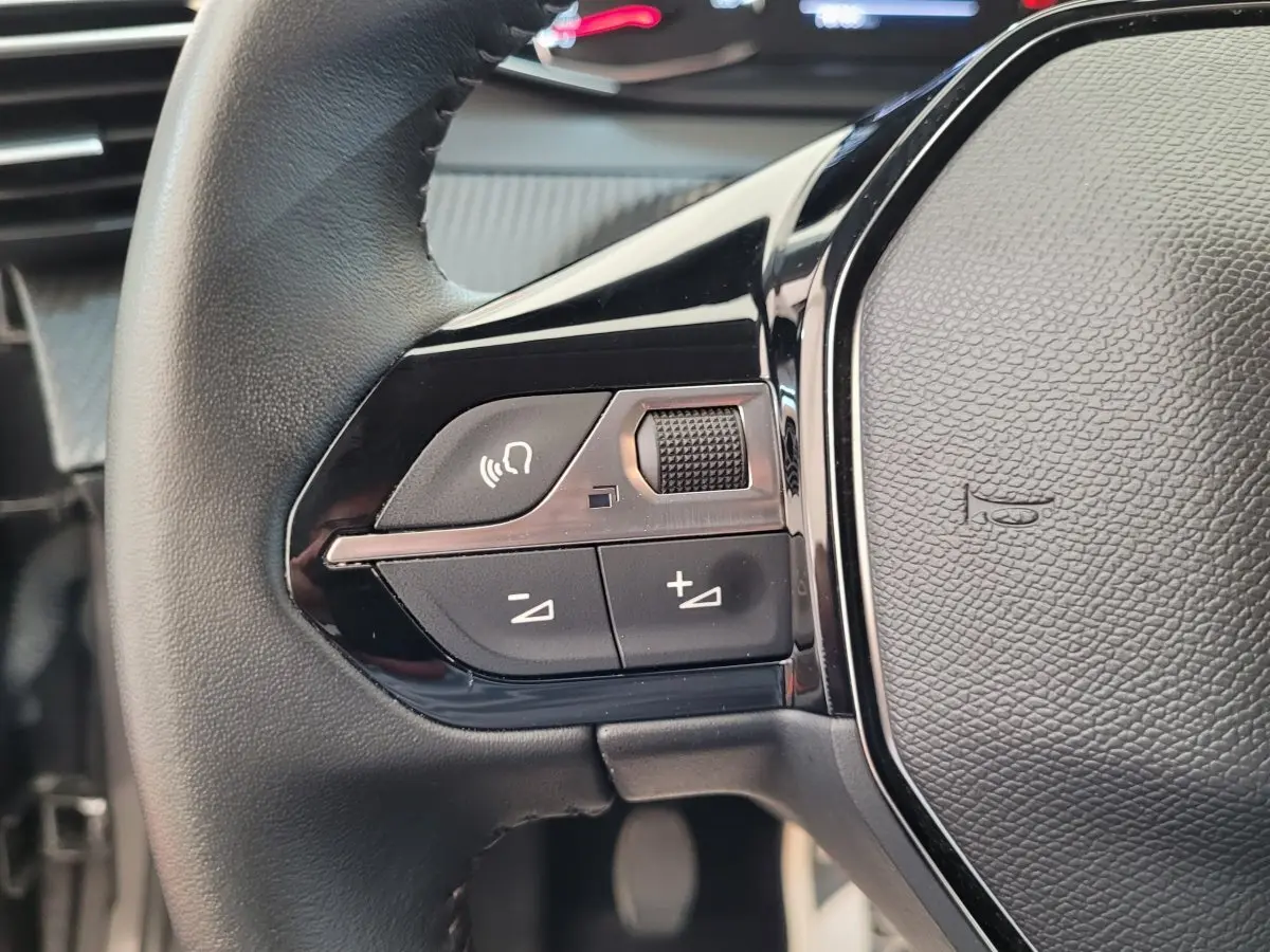Gros plan sur la partie gauche du volant cuir de la Peugeot 208 gris foncé avec commandes vocales et volume.