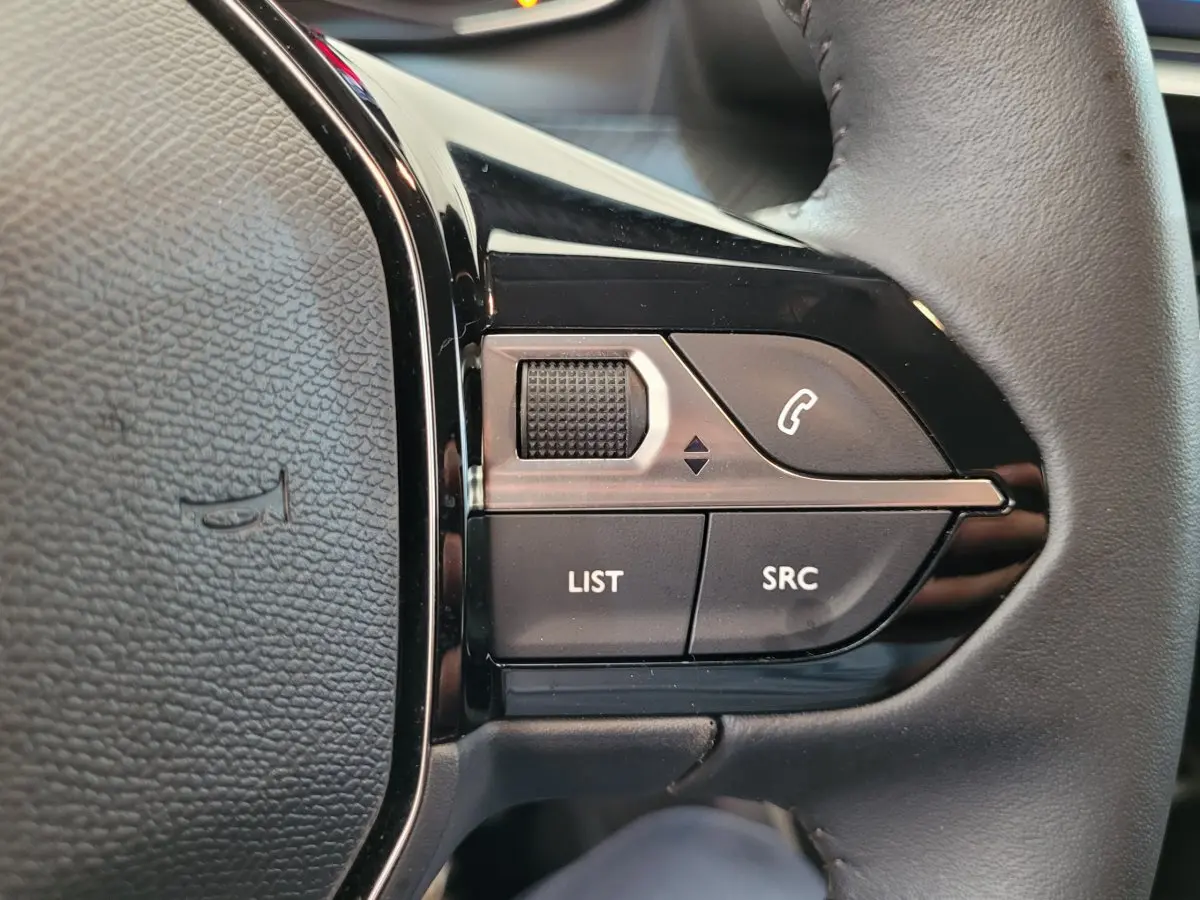 Gros plan sur les commandes gauche du volant cuir de la Peugeot 208 gris foncé 2023, avec boutons multifonctions.