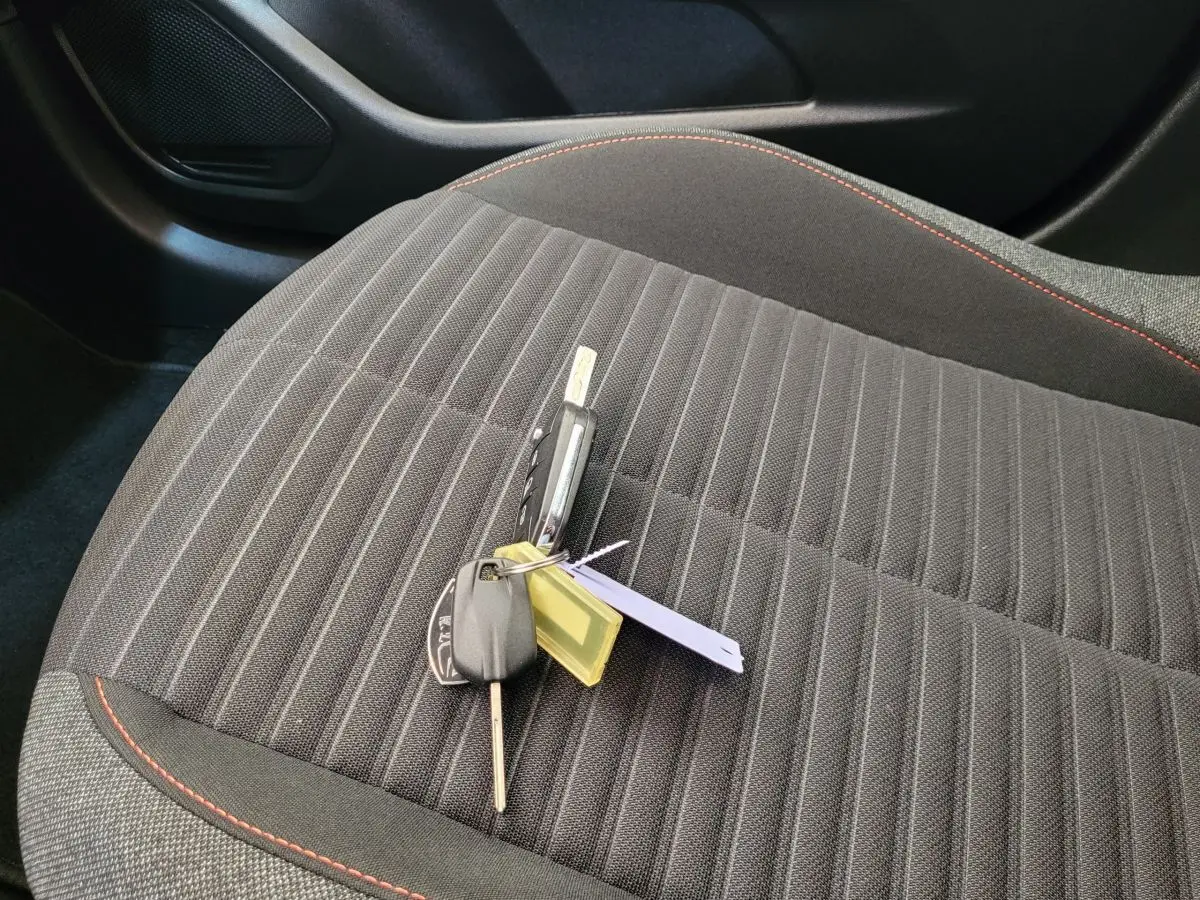 Clé de voiture posée sur le siège avant droit en tissu gris foncé avec surpiqûres rouges d'une Peugeot 208 2023.