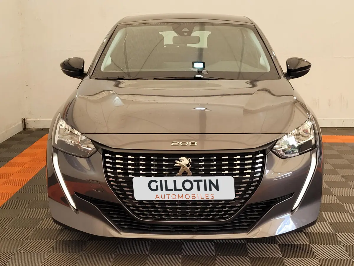 Vue frontale d'une Peugeot 208 gris foncé avec calandre noire et feux LED en forme de griffes.