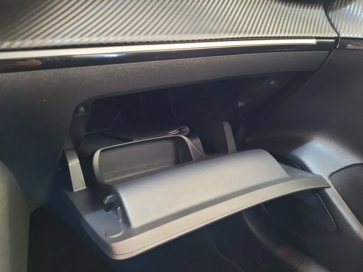 Intérieur du coffre à gants ouvert de la Peugeot 208 gris foncé, montrant le tableau de bord avec finition carbone.