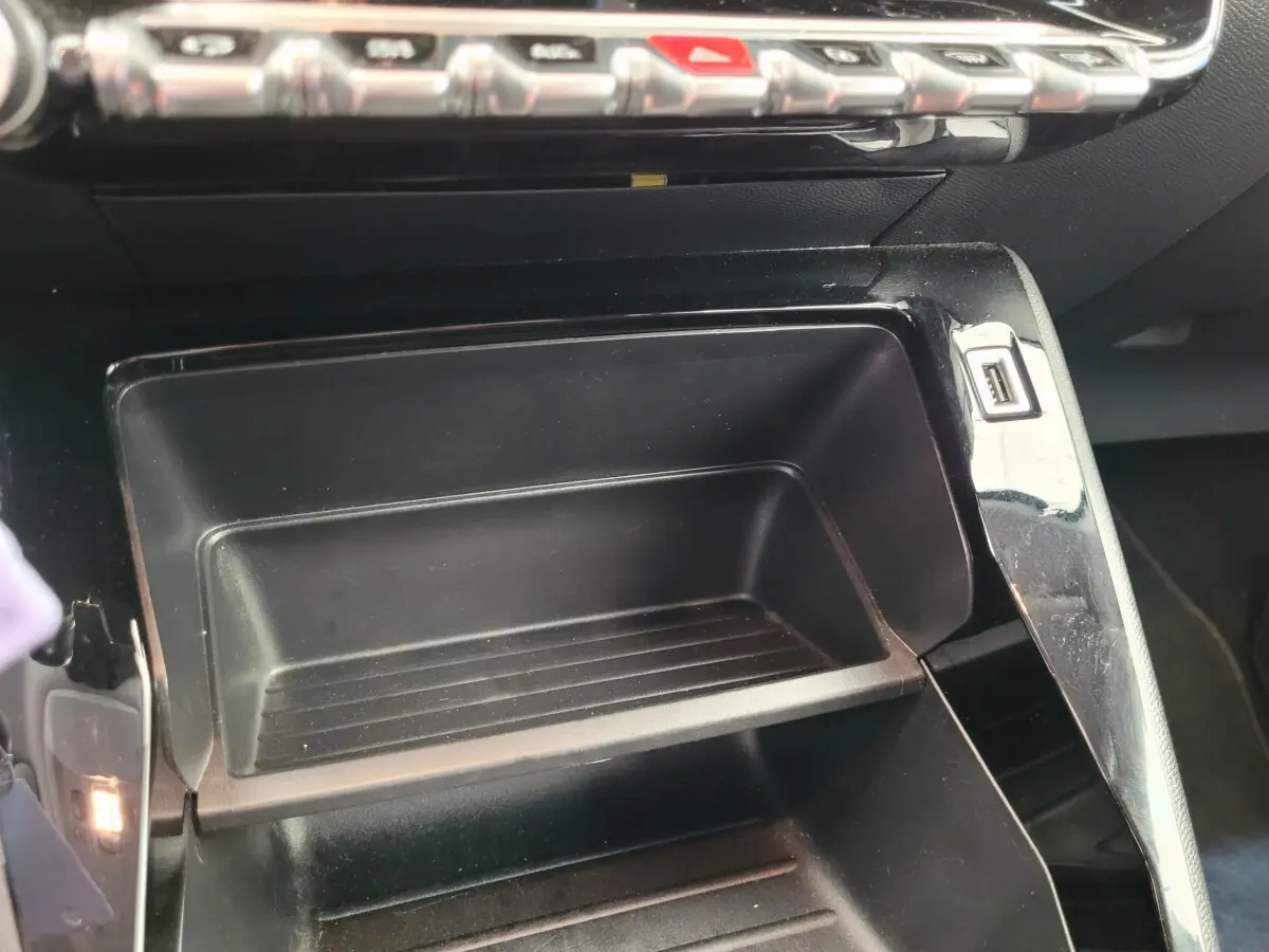 Gros plan sur le rangement central noir avec port USB du tableau de bord de la Peugeot 208 gris foncé 2023.