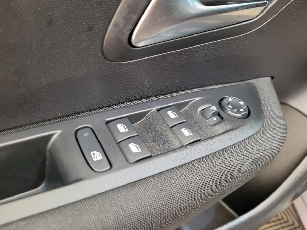 Gros plan sur les commandes de lève-vitres et réglages des rétroviseurs côté conducteur d’une Peugeot 208 gris foncé 2023.