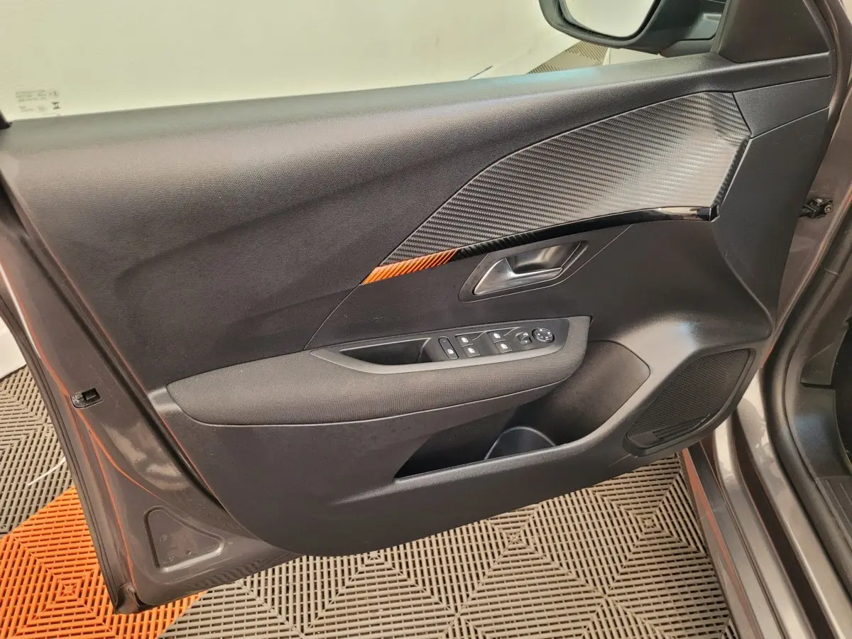 Vue intérieure côté gauche de la porte avant gris foncé de la Peugeot 208 avec inserts noirs et commandes électriques.