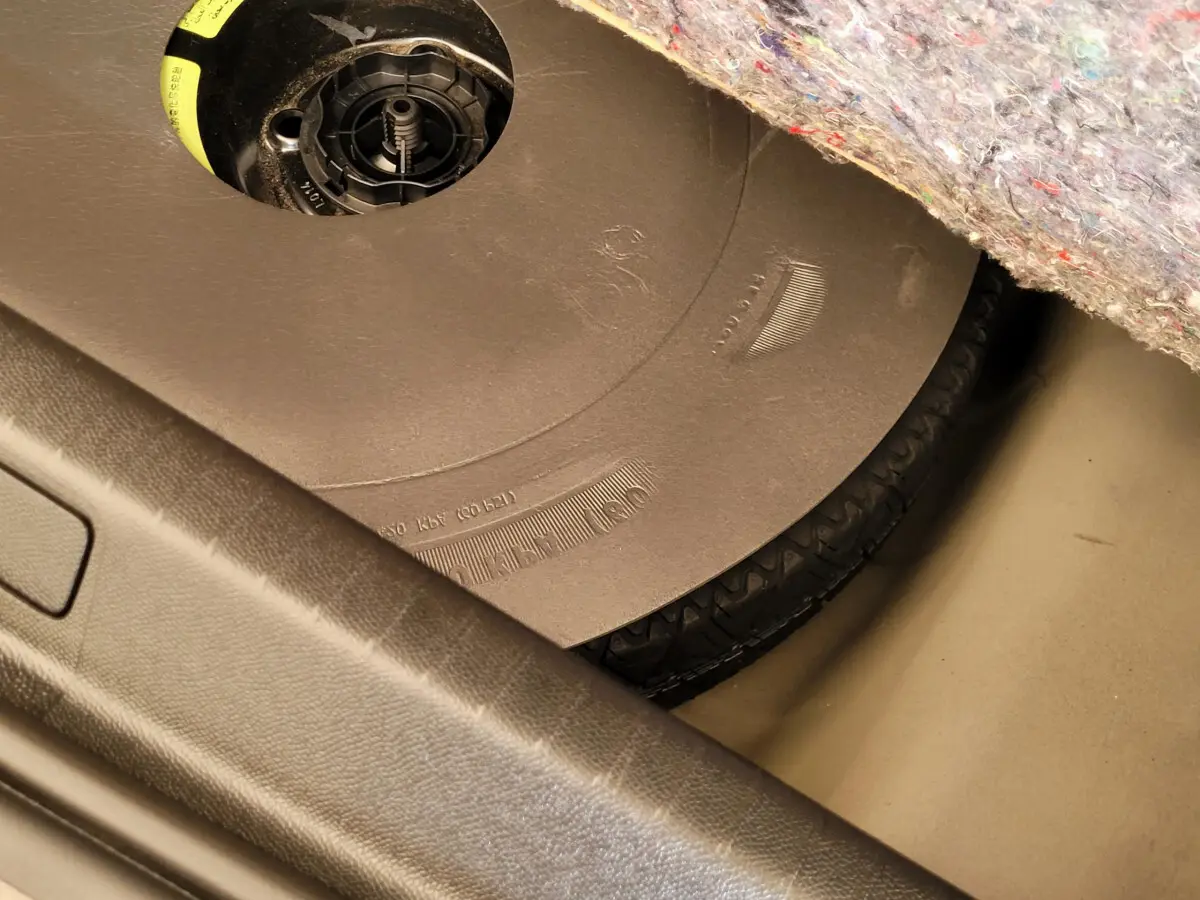 Gros plan sur la roue de secours sous la moquette du coffre d'une Peugeot 208 gris foncé 2023.