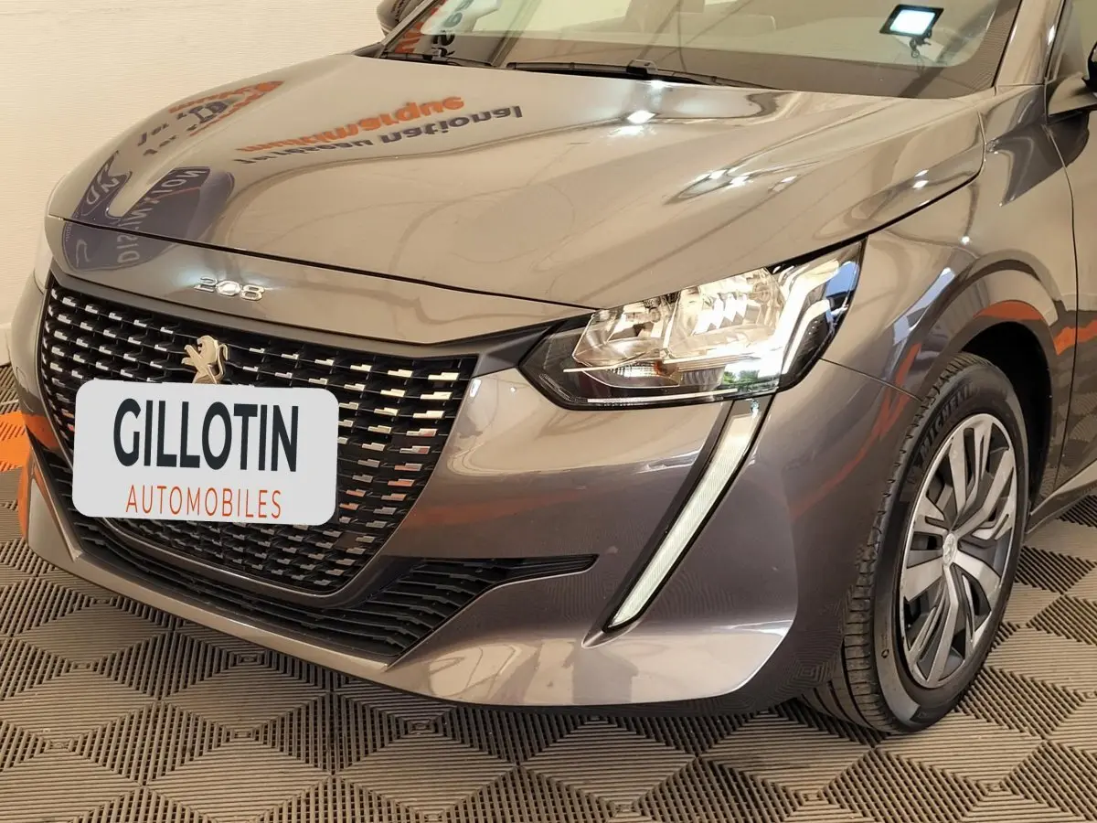 Vue 3/4 avant droit d'une Peugeot 208 gris foncé avec calandre distinctive et phares LED en forme de griffes.