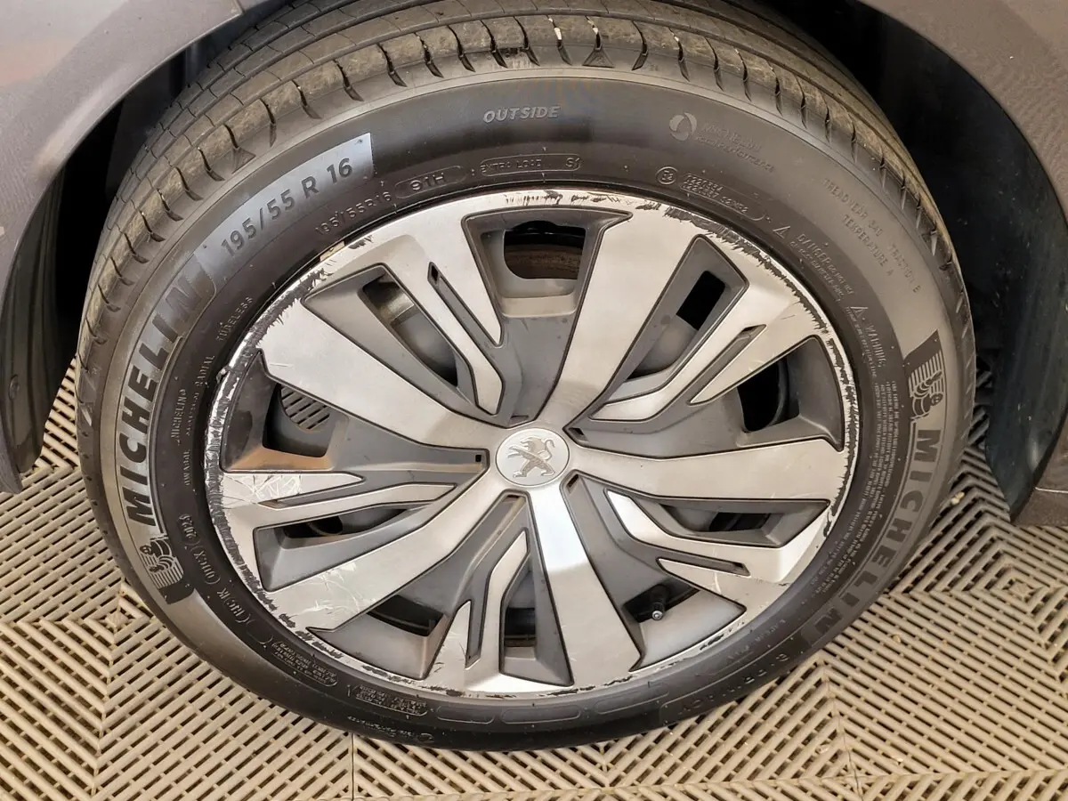 Gros plan sur la roue avant droite d'une Peugeot 208 gris foncé avec jante alliage au design moderne.