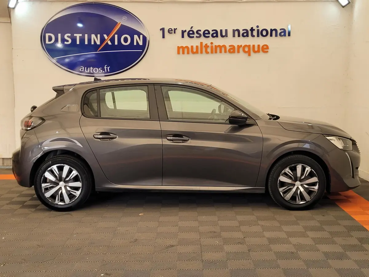 Profil côté gauche d'une Peugeot 208 BlueHDi 100 S&S Active Pack gris foncé, en intérieur avec logo Distinxion en arrière-plan.