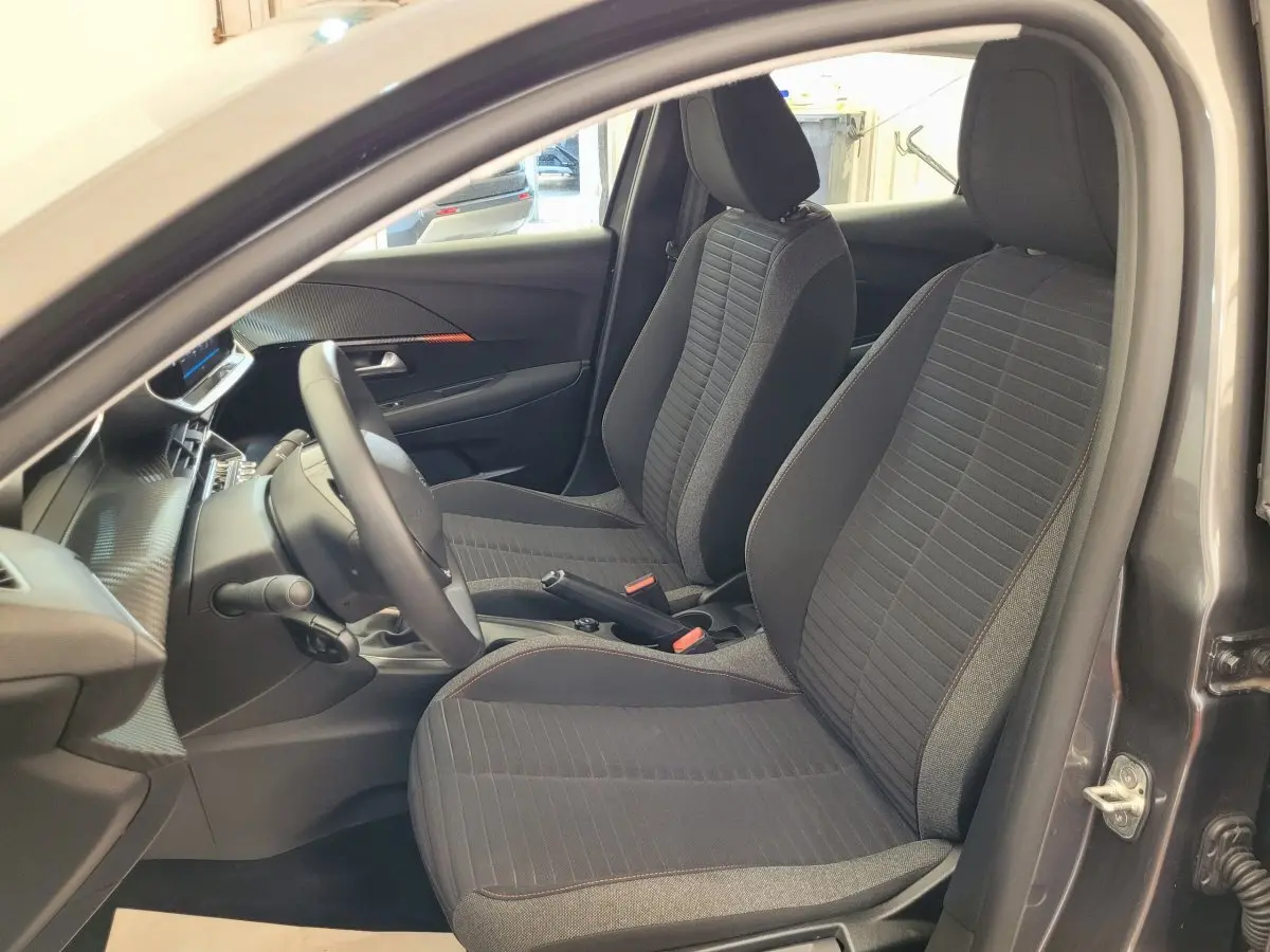 Vue intérieure côté conducteur de la Peugeot 208 BlueHDi 100 gris foncé, sièges tissu noir avec surpiqûres rouges.