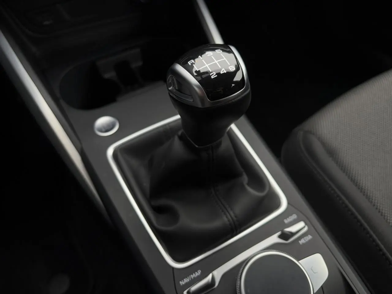 Gros plan sur le levier de vitesses manuel noir de l'Audi Q2 30 TFSI S-Line, entouré de commandes et tissu gris.