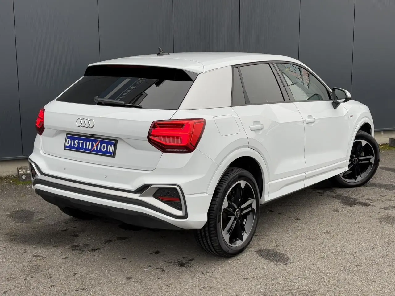 Audi Q2 blanc Glacier en 3/4 arrière droit, avec jantes noires polies et vitres surteintées.