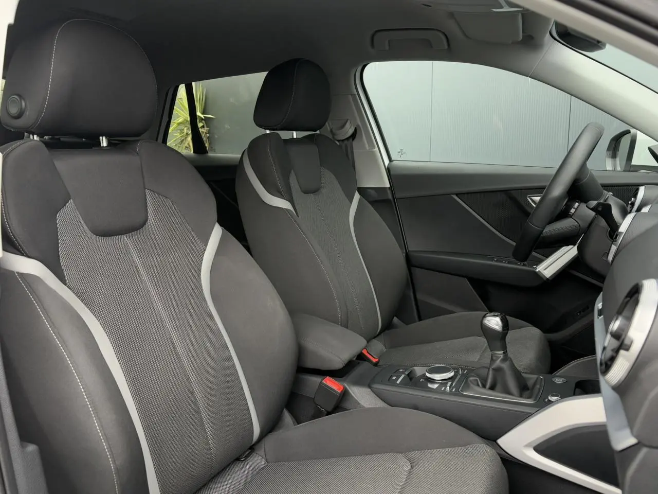 Vue intérieure côté avant droit de l’Audi Q2 30 TFSI S-Line 2024 avec sièges sport tissu gris et levier de vitesses manuel.