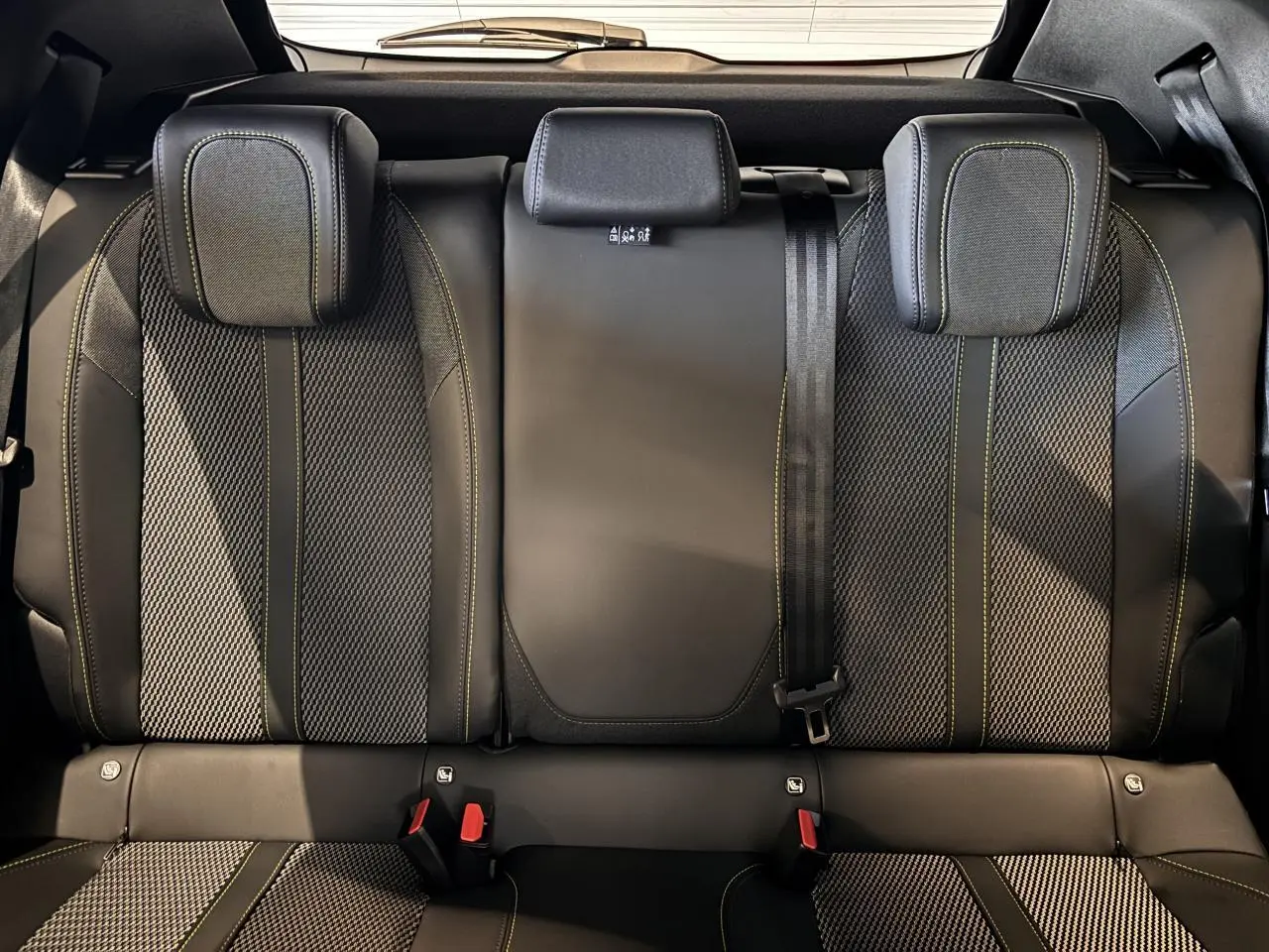 Vue intérieure arrière des sièges noirs avec surpiqûres vertes du Peugeot 2008 gris hybride 2025 GT Phase 2.