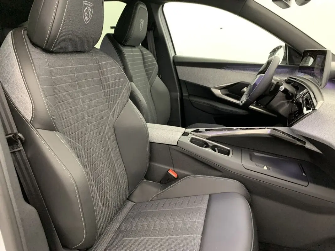 Gros plan sur la roue avant droite du Peugeot 3008 Hybrid blanc Okenite avec jante noire brillante et logo Peugeot central.