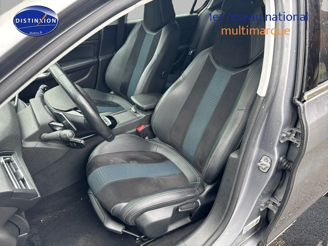 Vue intérieure côté conducteur de la Peugeot 308 gris Artense, sièges en tissu et cuir avec inserts bleus.