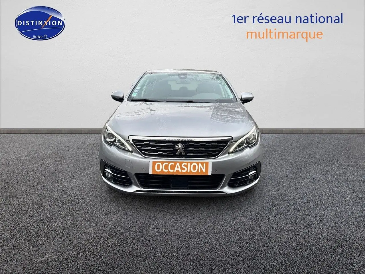 Vue frontale d'une Peugeot 308 gris Artense avec plaque "OCCASION" sur fond neutre.