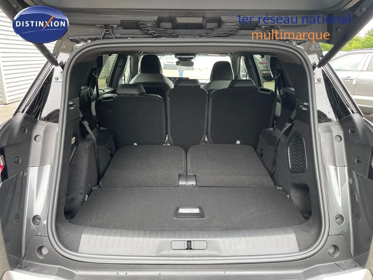 Coffre ouvert en vue arrière d'un Peugeot 5008 gris titane métal avec sièges arrière rabattus et toit noir visible.