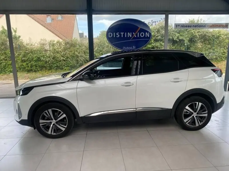 Profil côté gauche d'un Peugeot 3008 blanc nacré 2023 avec toit noir et jantes alliage en intérieur showroom.