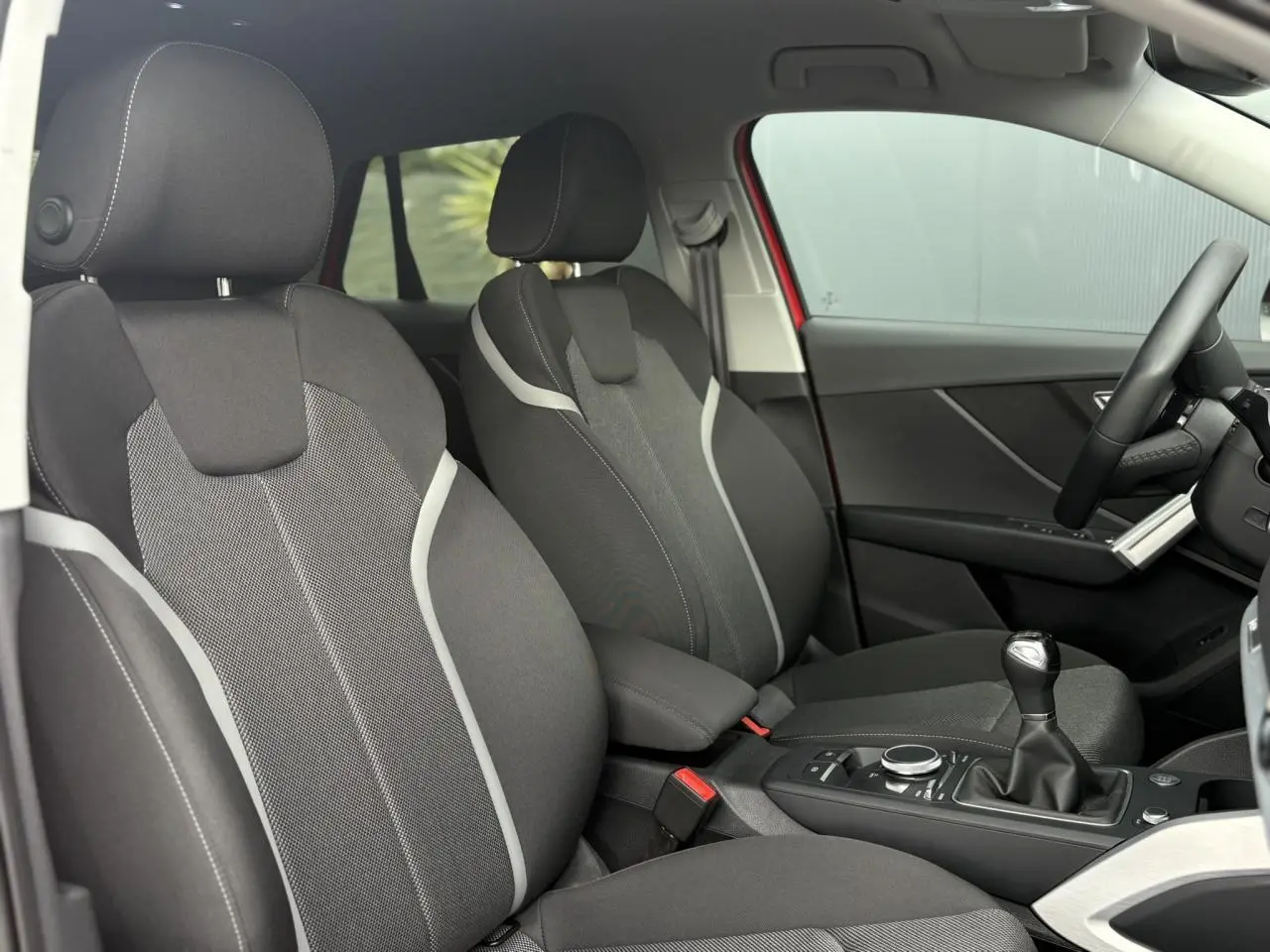 Vue intérieure côté droit de l'Audi Q2 30 TFSI S-Line 2024, sièges sport tissu gris avec surpiqûres claires et levier de vitesses manuel.