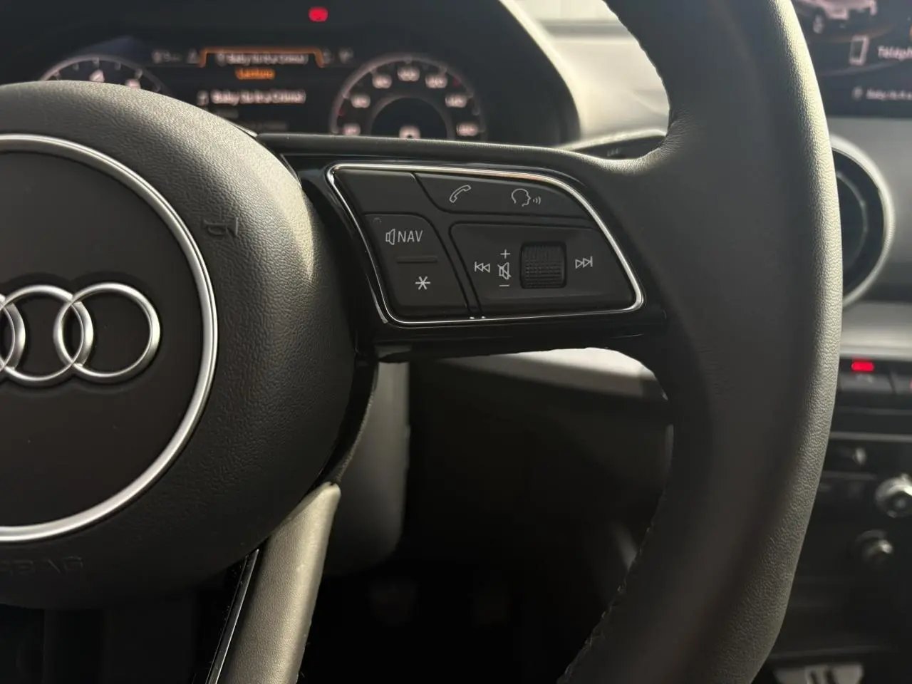 Gros plan sur le volant multifonction noir de l'Audi Q2 30 TFSI S-Line avec commandes audio et navigation visibles.