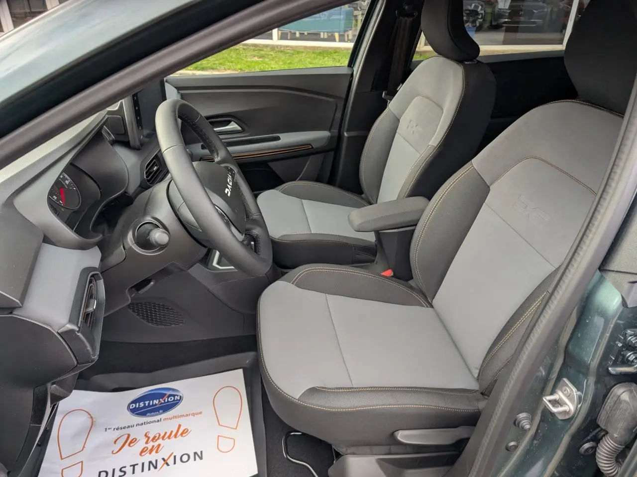 Intérieur avant droit du Dacia Jogger 2025 vert métallisé, sièges TEP gris clair avec surpiqûres brun cuivré.