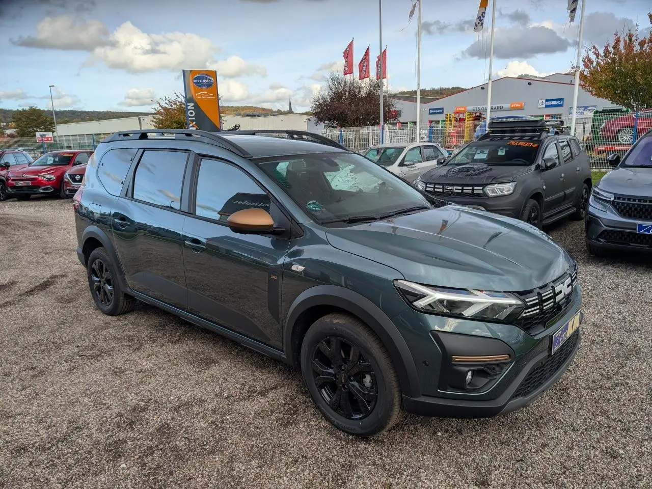 Dacia Jogger vert métallisé en vue 3/4 avant droit avec rétroviseurs brun cuivré et jantes noires.