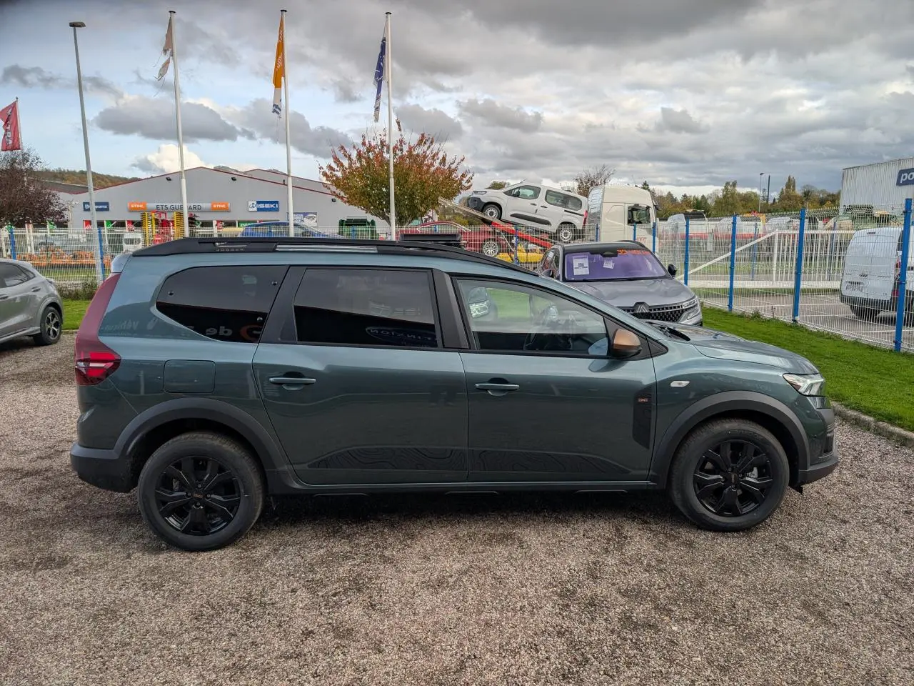 Profil côté gauche du Dacia Jogger 2025 vert métallisé avec jantes noires et barres de toit noires.