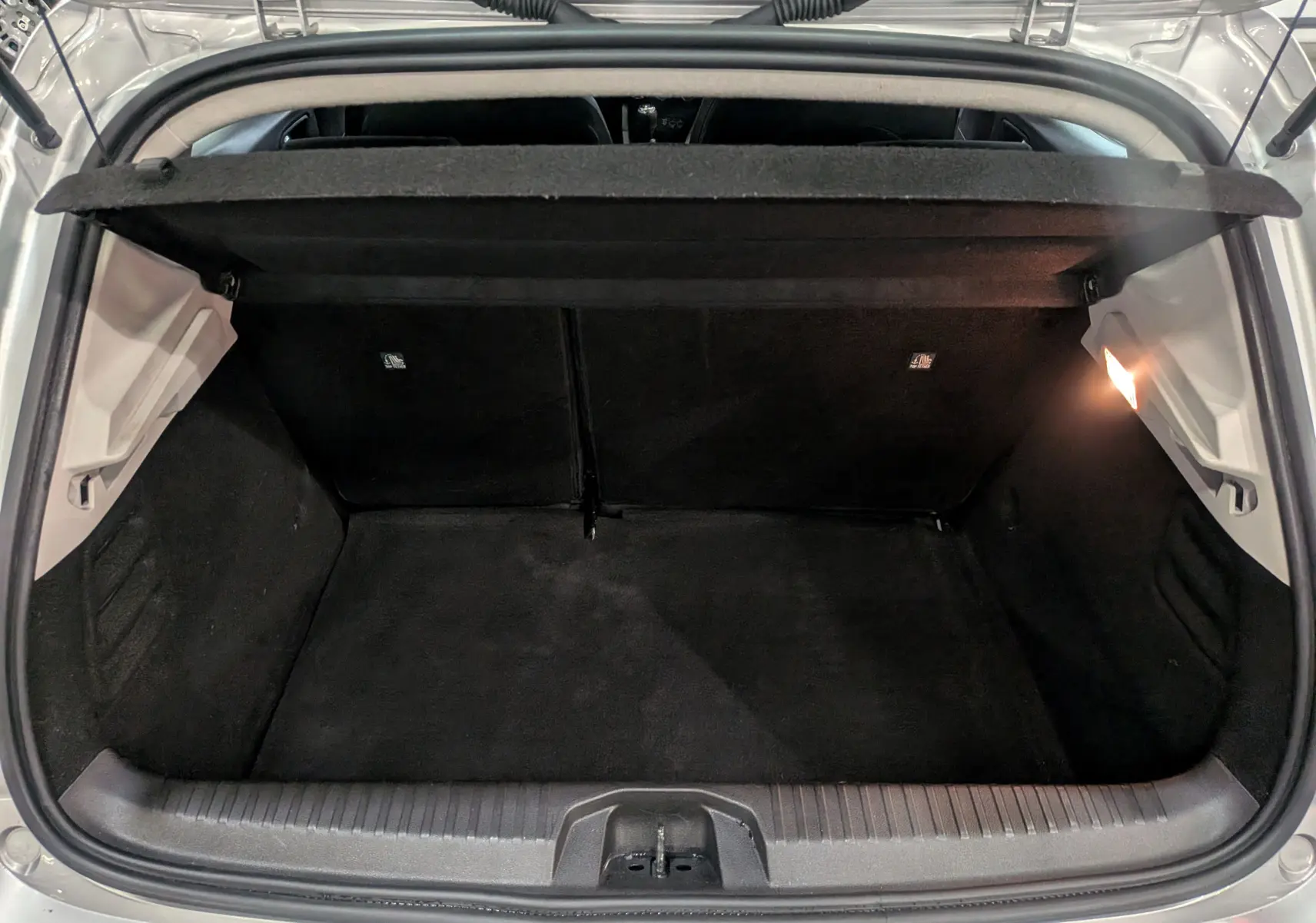 Vue intérieure du coffre ouvert d'une Renault Clio V gris platine, montrant l'espace de rangement et l'éclairage latéral.