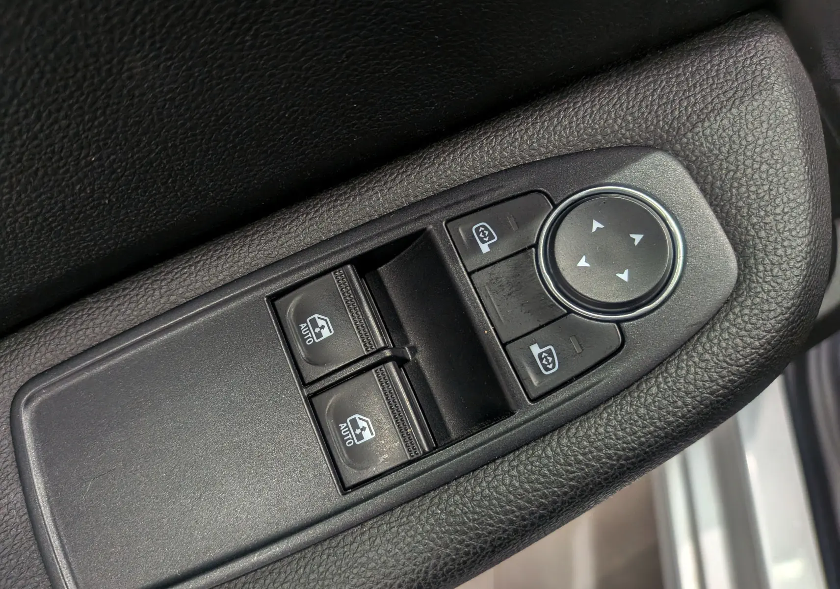 Gros plan sur les commandes de lève-vitres et réglage des rétroviseurs côté conducteur d’une Renault Clio V gris platine.