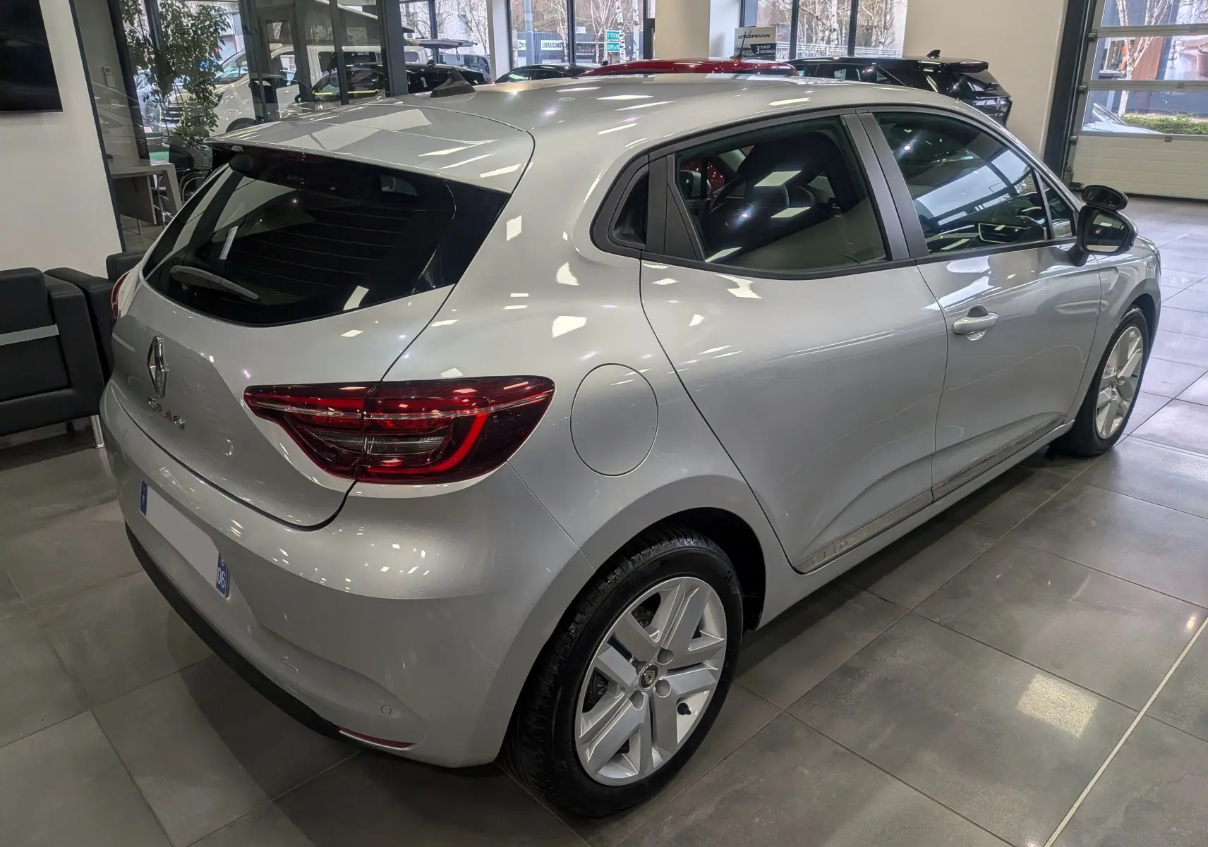 Vue 3/4 arrière droite d'une Renault Clio V gris platine en showroom, avec feux arrière LED et jantes alliage visibles.