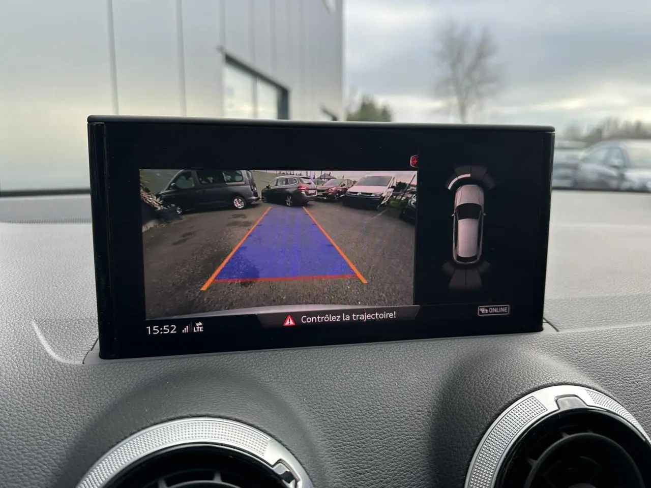 Écran intérieur montrant la caméra de recul avec guidage de trajectoire d’un Audi Q2 argent rosé, vue avant du tableau de bord.