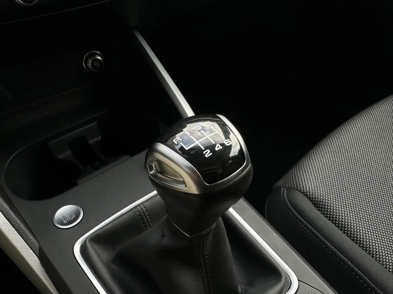 Gros plan sur le levier de vitesses manuel noir et argenté de l'Audi Q2 30 TFSI 110 S-Line 2024, intérieur sombre.