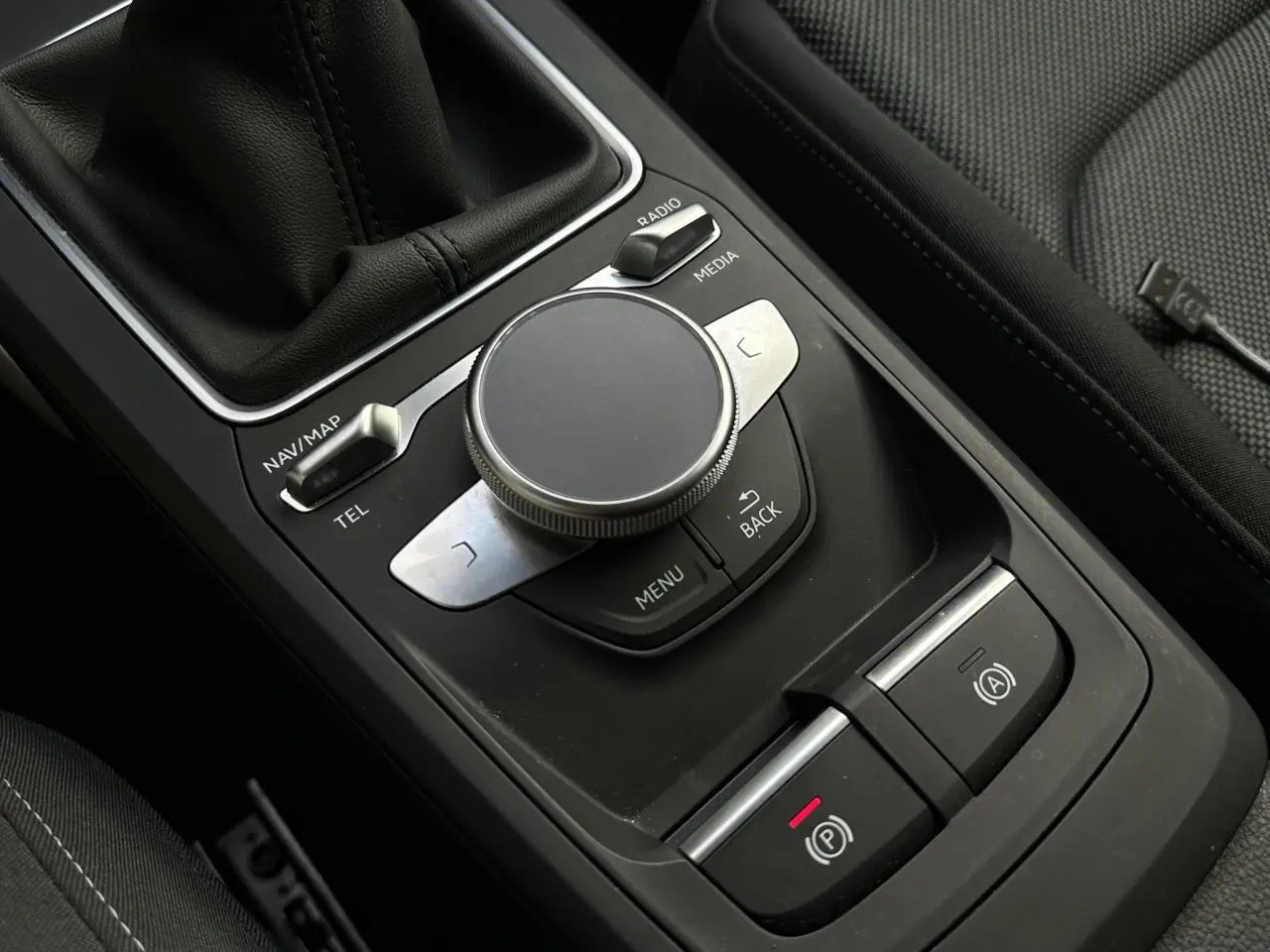 Vue rapprochée de la console centrale noire de l'Audi Q2 30 TFSI S-Line 2024 avec commandes multimédia et frein électrique.