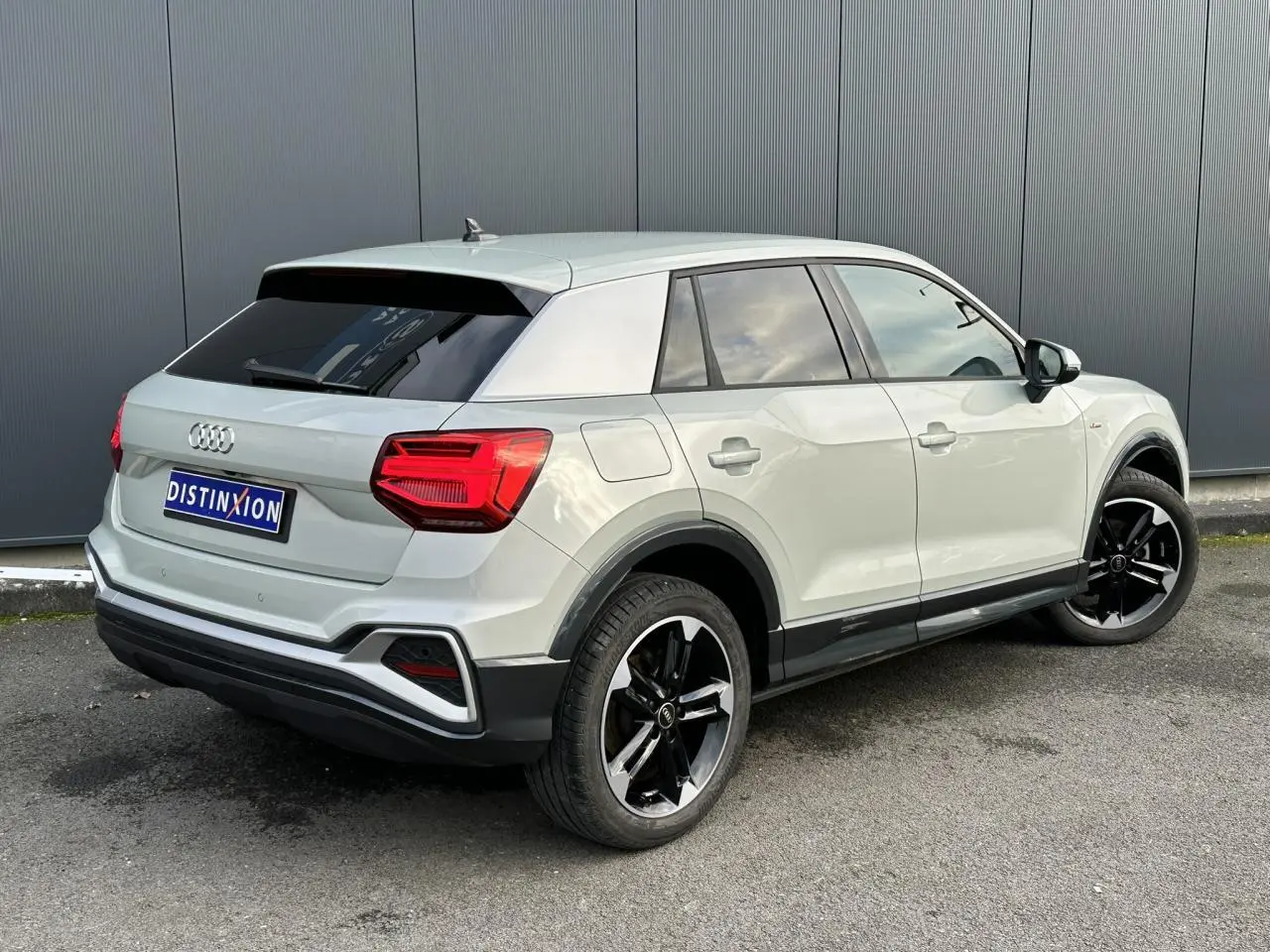 Audi Q2 30 TFSI S-Line argent rosé, vue 3/4 arrière droit, jantes noires brillantes et vitres surteintées.