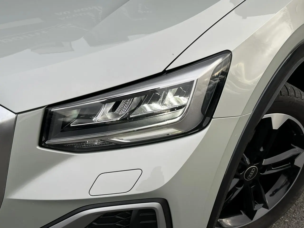 Gros plan sur le phare avant droit et la jante noire polie d’un Audi Q2 30 TFSI S-Line argent rosé.