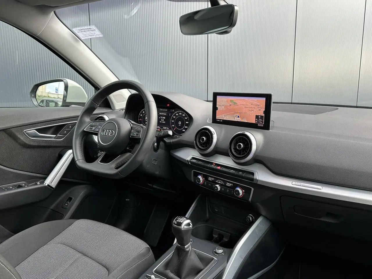 Vue intérieure côté conducteur de l'Audi Q2 30 TFSI S-Line 2024, avec volant cuir, écran navigation et levier de vitesse manuel.