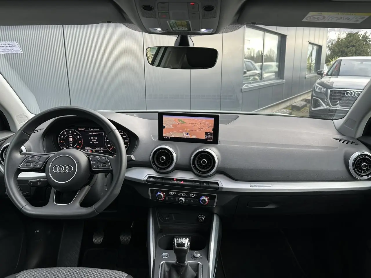 Vue intérieure de l'Audi Q2 30 TFSI S-Line 2024, tableau de bord avec écran central et volant multifonction cuir.