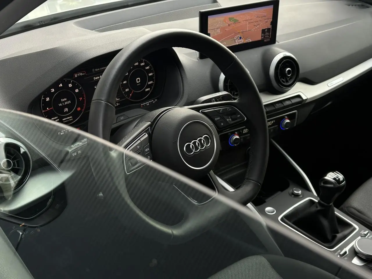 Vue intérieure côté conducteur de l'Audi Q2 30 TFSI S-Line 2024, volant cuir, écran navigation et levier de vitesses manuel.