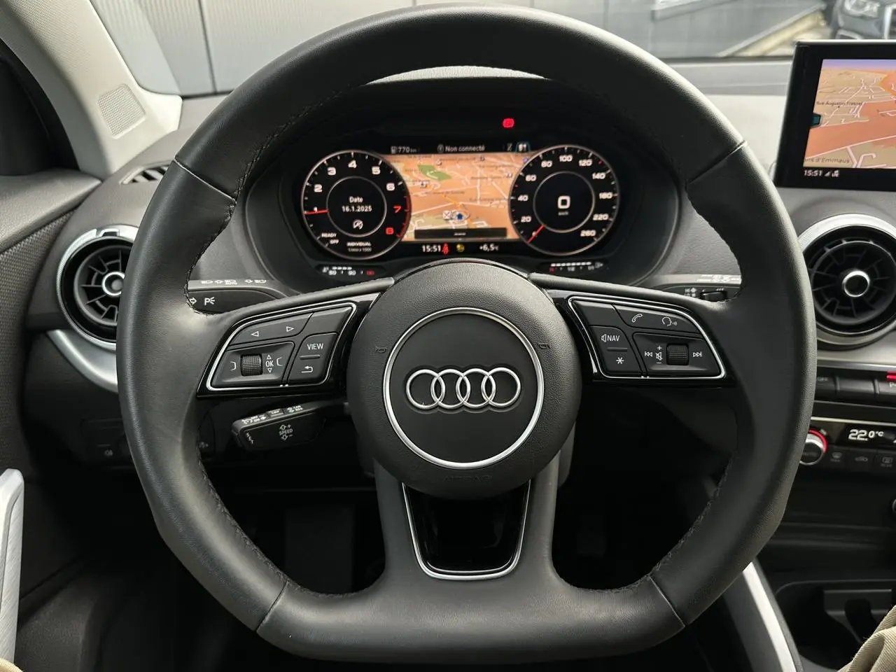 Vue rapprochée du volant cuir noir multifonction et du tableau de bord numérique de l'Audi Q2 argent rosé 2024.