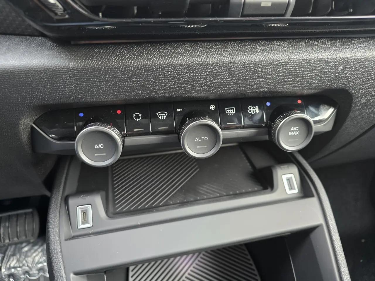 Vue rapprochée de la console centrale noire de la Citroën C4 hybride 2025, avec commandes climatisation et ports USB visibles.