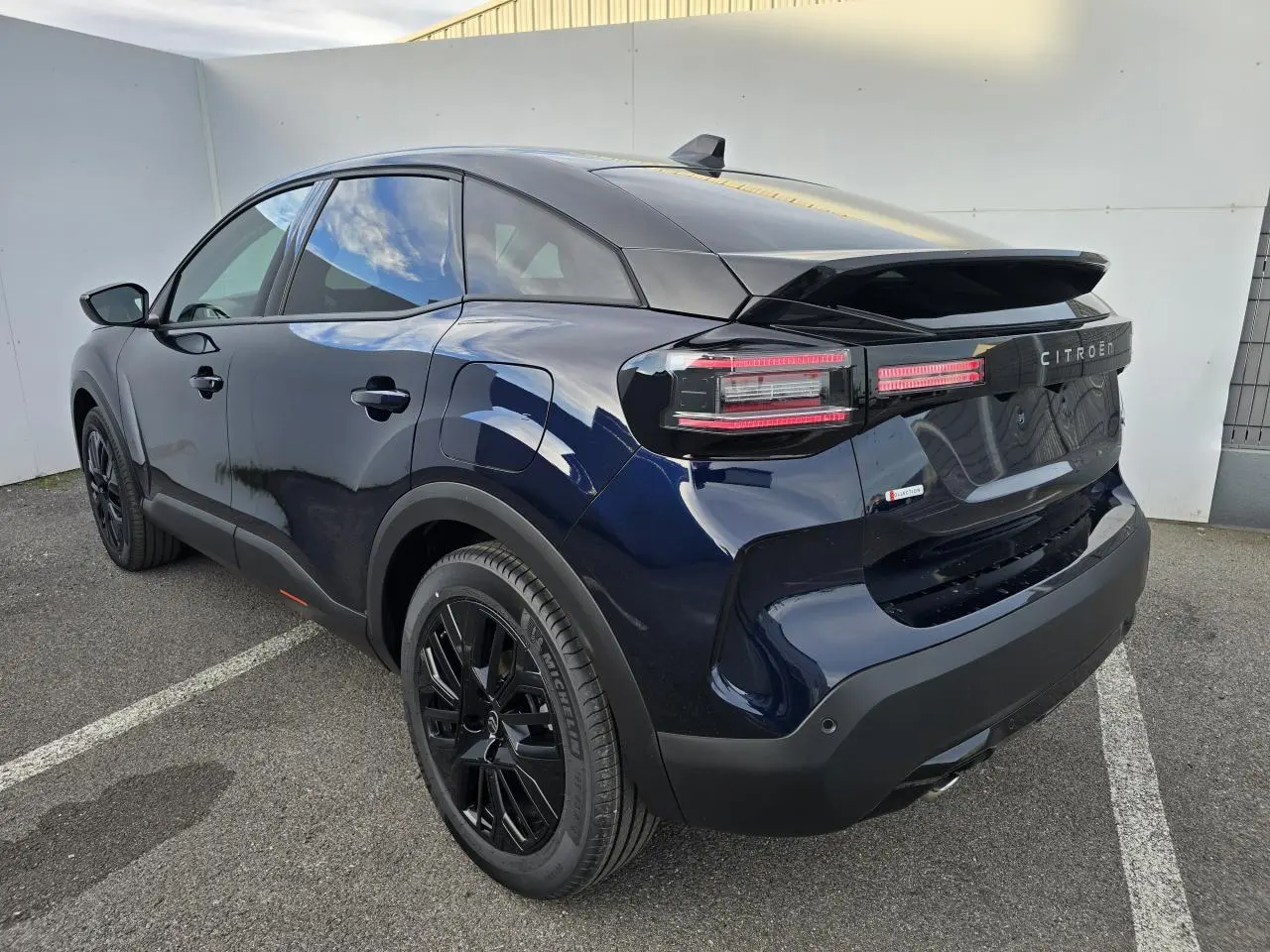 Vue 3/4 arrière droite d'une Citroën C4 III hybride bleu éclipse avec toit noir et jantes noires brillantes