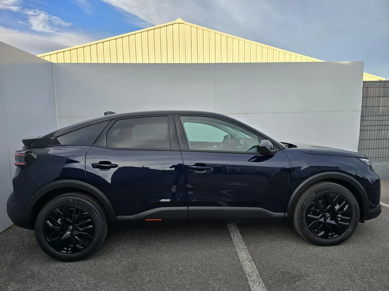 Profil côté gauche de la Citroën C4 III hybride 2025 en bleu eclipse avec toit noir et jantes noires.