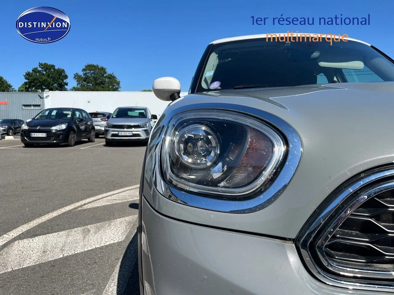 Gros plan sur le phare avant gauche et la calandre chromée d'une MINI Countryman Moonwalk Grey, toit et rétroviseurs blancs.
