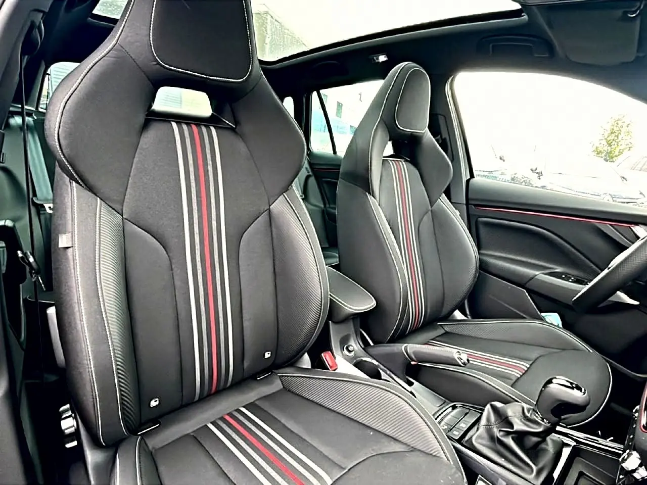 Vue intérieure du Skoda Kamiq Monte Carlo 2026 montrant les sièges sport noirs avec bandes rouges et blanches et toit panoramique.
