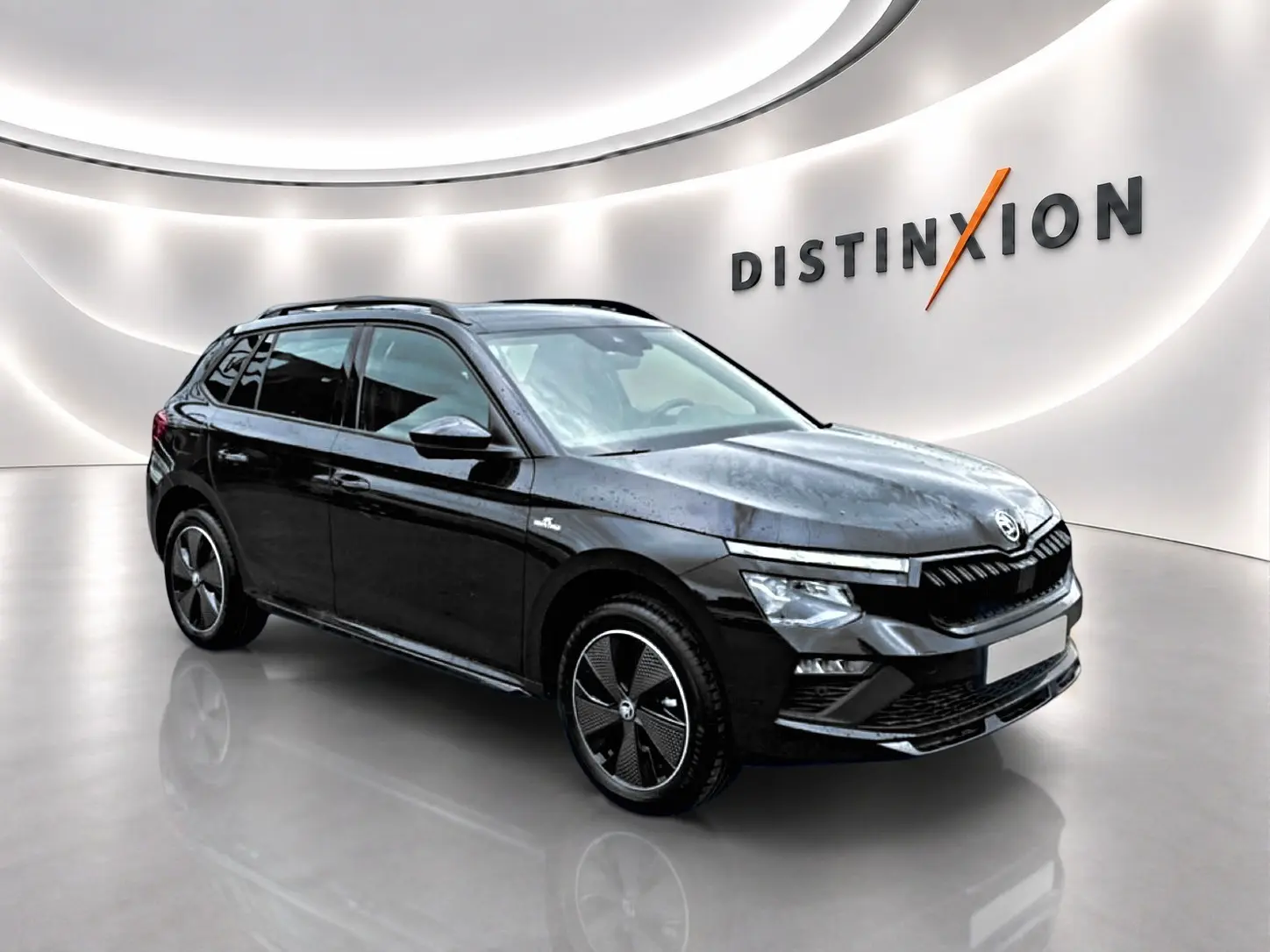Vue 3/4 avant droite d'un Skoda Kamiq noir avec jantes alu noires, dans un showroom lumineux au mur blanc.
