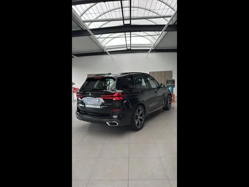 BMW X5 xDrive50e noir en 3/4 arrière droit, avec échappement chromé et jantes alliage 21 pouces en showroom.