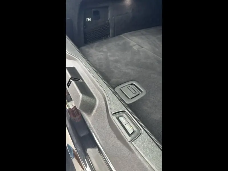 Détail du coffre noir du BMW X5 xDrive50e 2023 avec bouton d'ouverture électrique et revêtement en tissu.